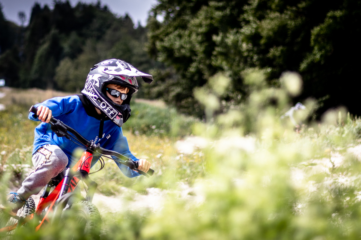 Young mountain biker in a blue jersey cornering on an orange downhill bike at Bike Park Kranjska Gora