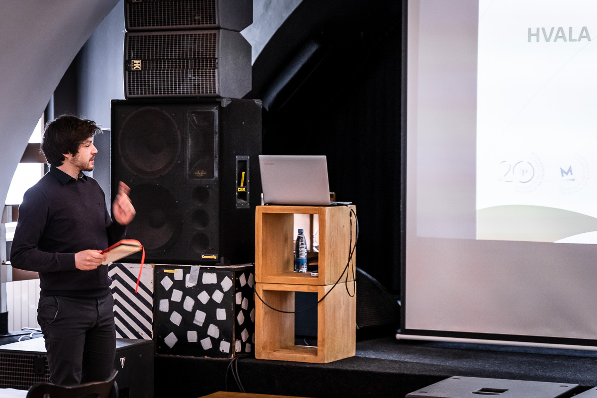 Grega Donša speaking beside a lectern at MIKK Murska Sobota, with the closing slide reading HVALA on the screen behind him