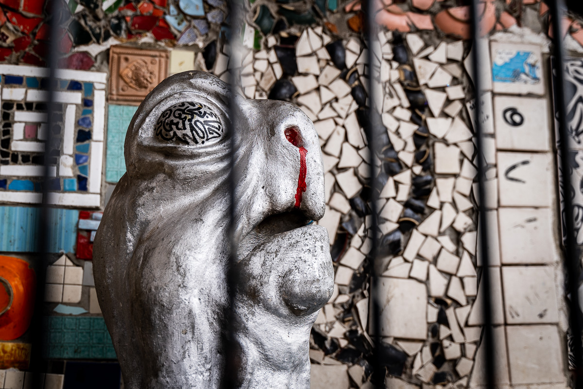 Unusual sculpted face seen behind metal bars at Metelkova