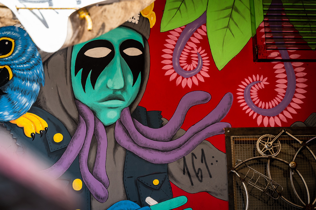 Colourful mural with a blue bird and masked figure at Metelkova