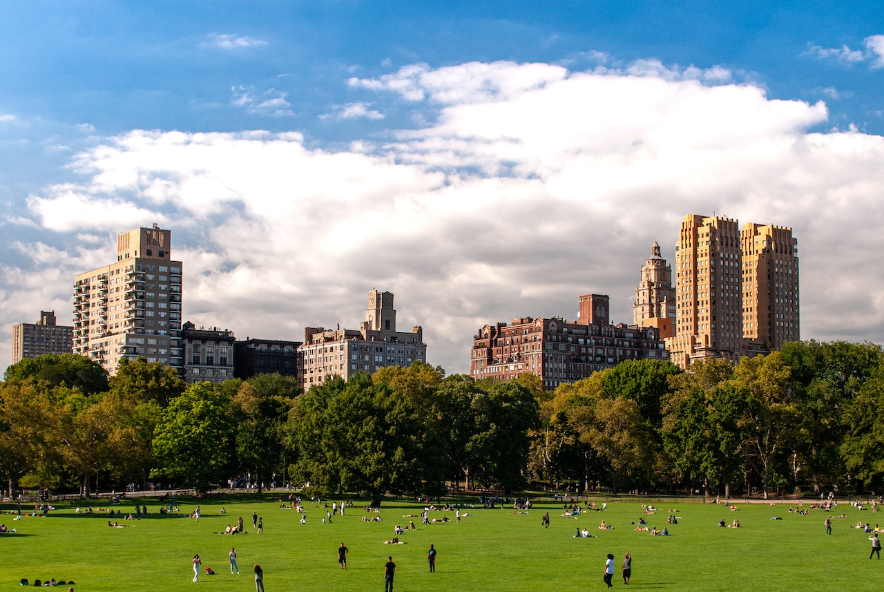 People crossing Sheep Meadow beneath a broad sky and the Upper West Side skyline
