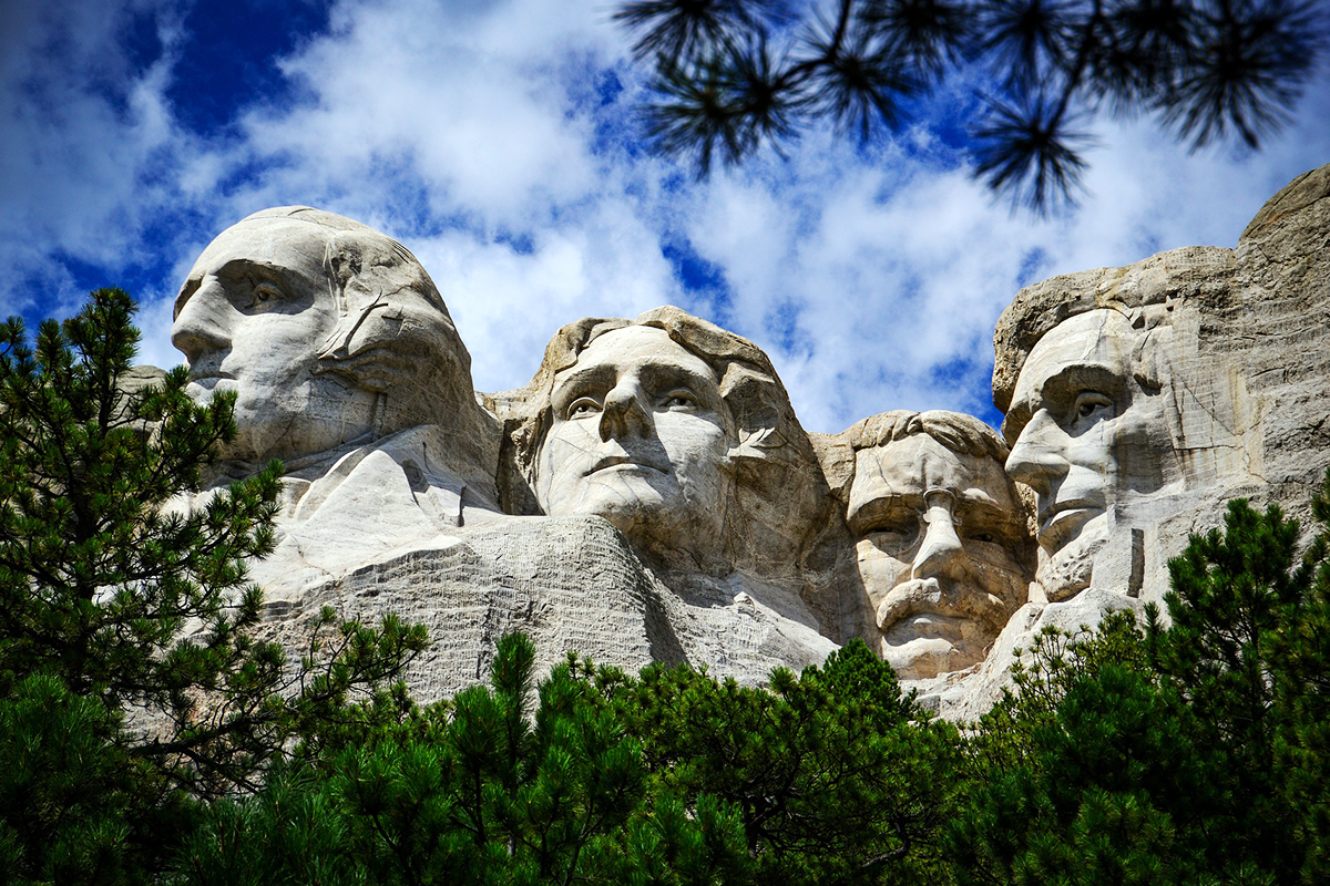 Mount Rushmore viewed through dark ponderosa pine branches beneath moving cloud
