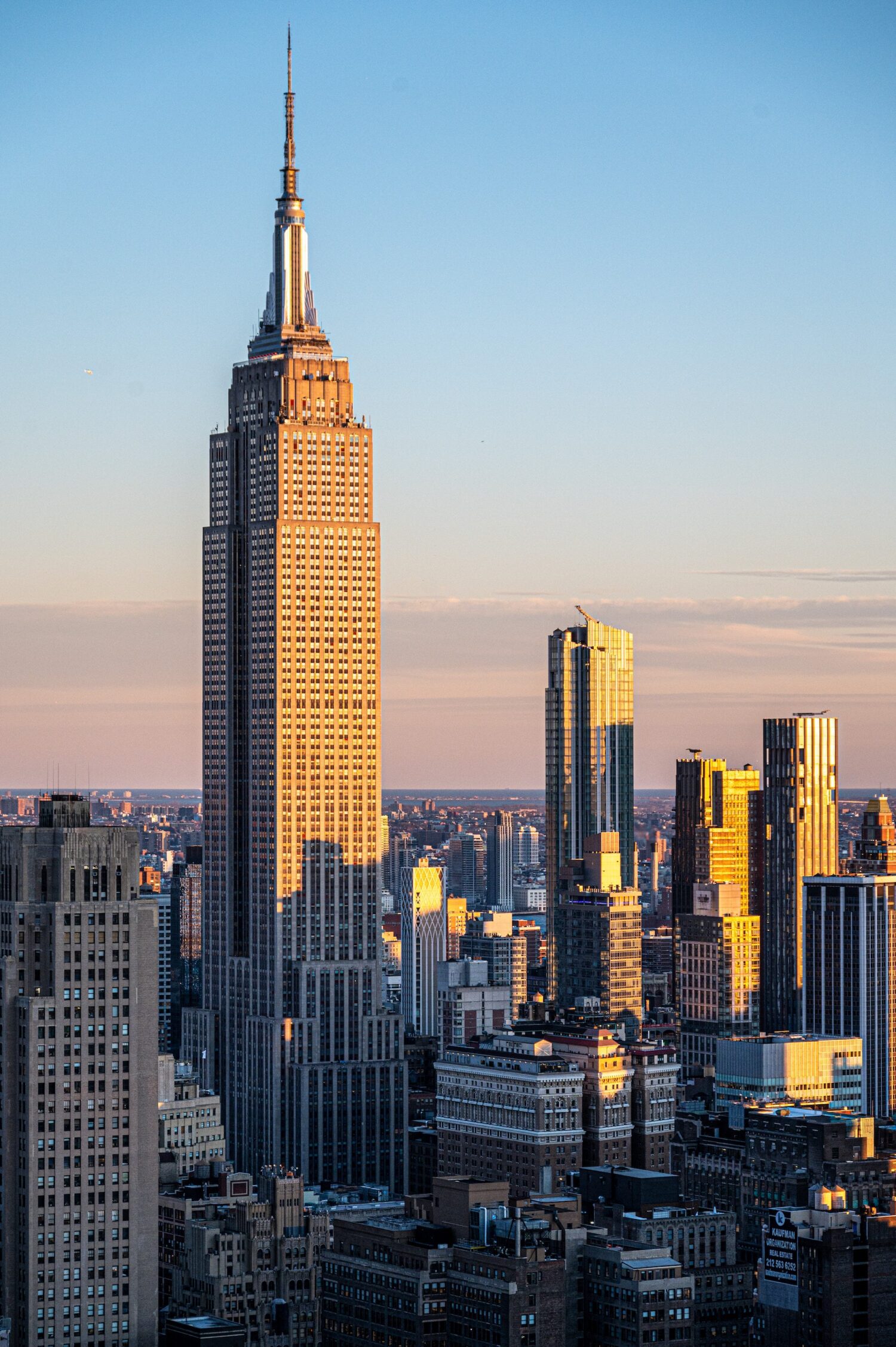 Vertical portrait of the Empire State Building in warm light above surrounding Midtown towers
