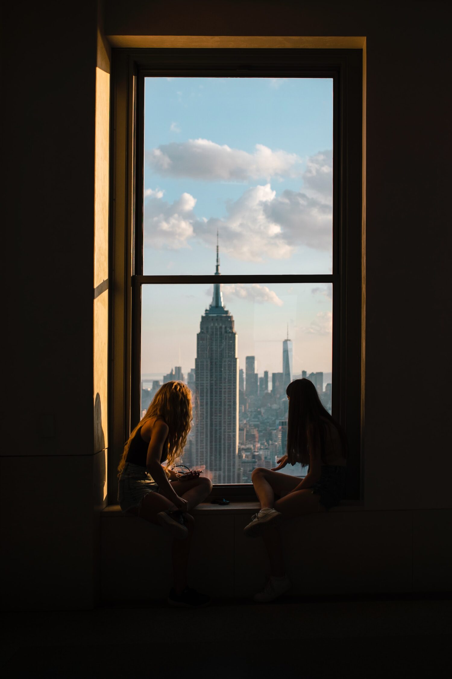 Empire State Building framed by a dark window with two people sitting in silhouette