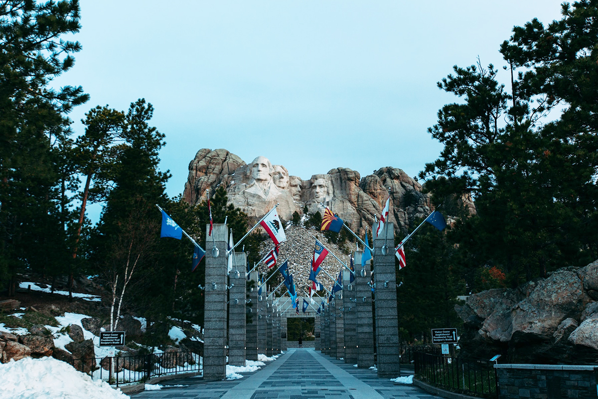 Avenue of Flags leading toward Mount Rushmore with snow beside the walkway