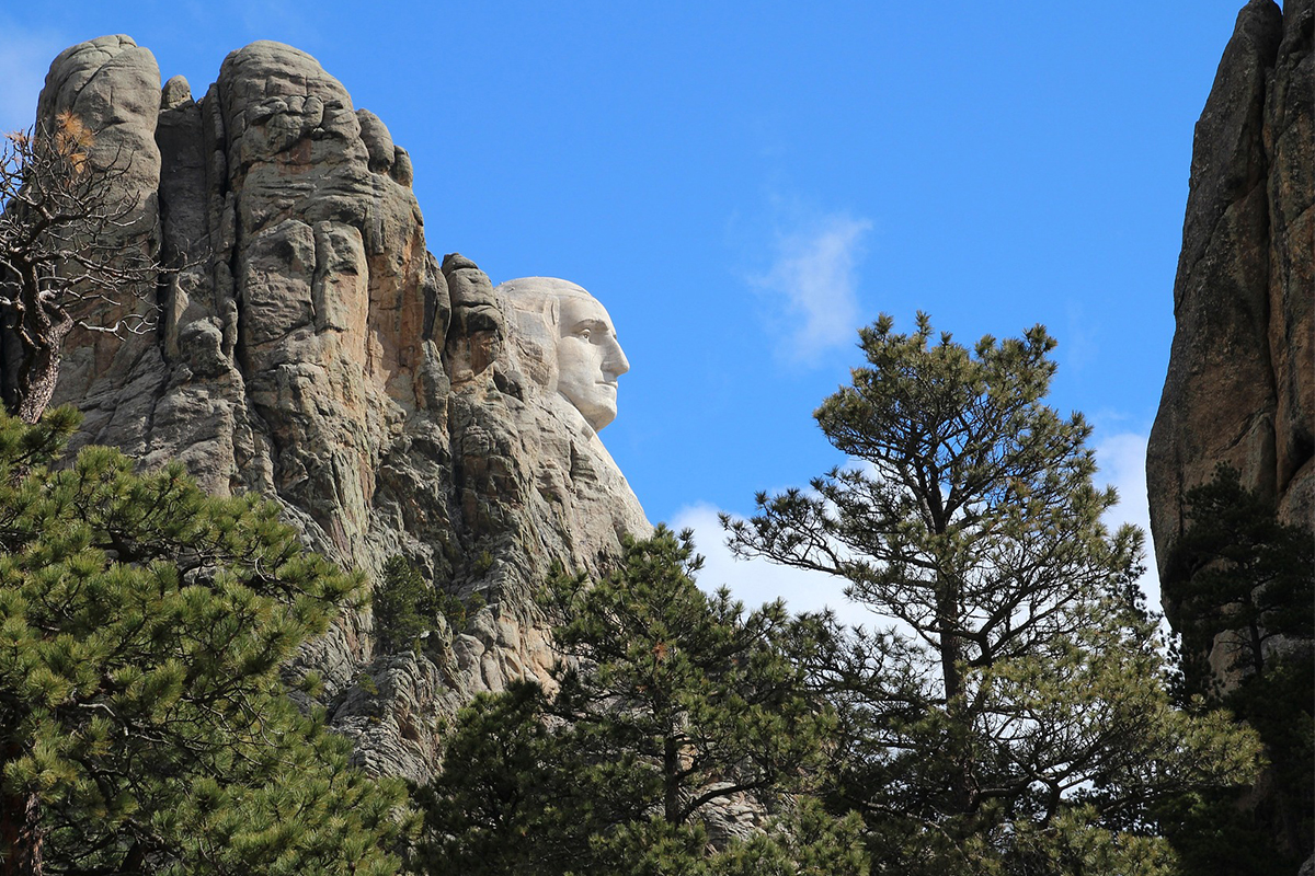 Side profile of George Washington at Mount Rushmore framed by granite and pine trees