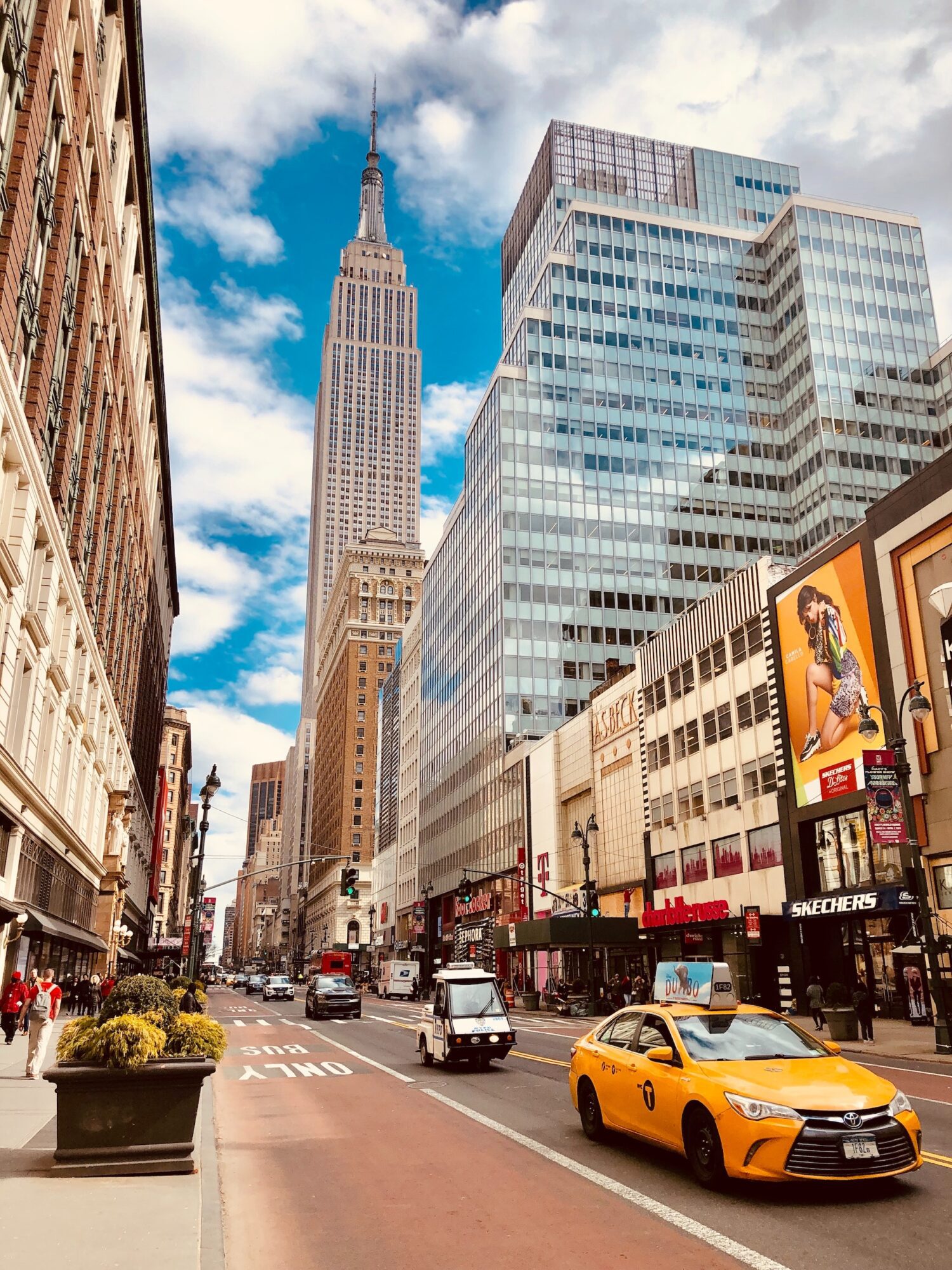 Empire State Building seen from a Midtown avenue above traffic, shops and a yellow taxi