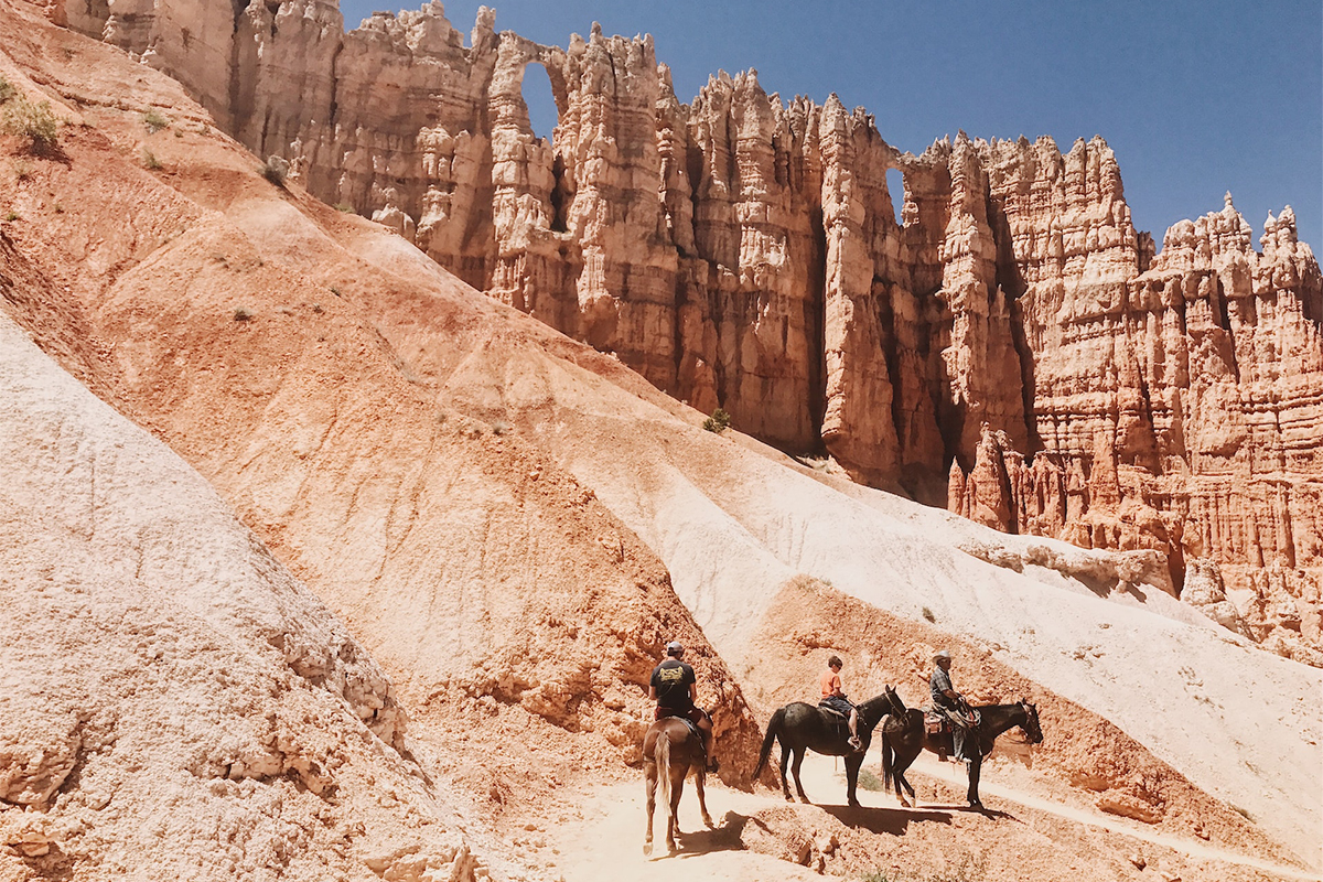 Riders and horses passing below the Wall of Windows in Bryce Canyon