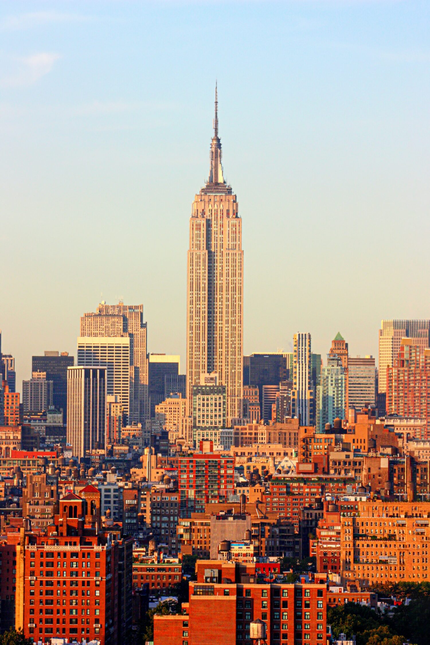 Empire State Building illuminated by golden-hour light above layers of Manhattan rooftops