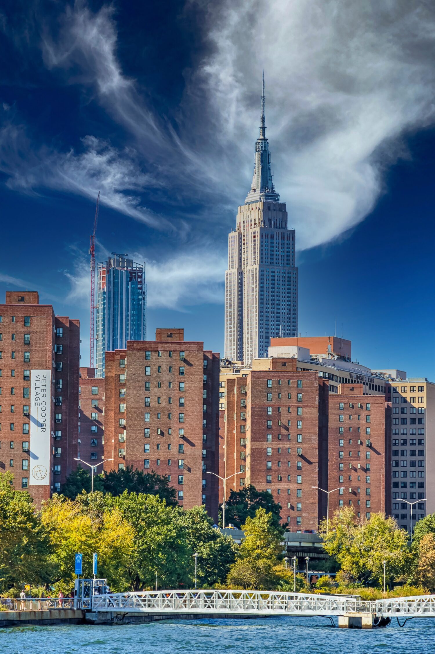 Distant view of the Empire State Building above foreground apartments, trees and a dramatic sky