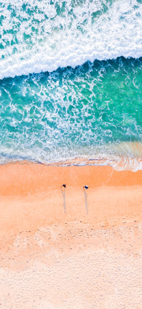 Aerial beach wallpaper with turquoise surf, warm sand and a small person walking near the water