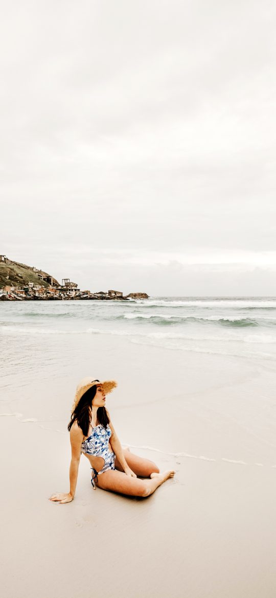 Woman sitting on a pale beach and looking toward a calm sea