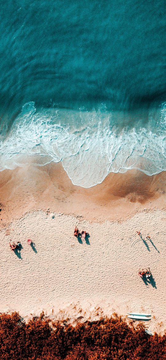 Vertical drone photograph of a beach with small groups of people near the water