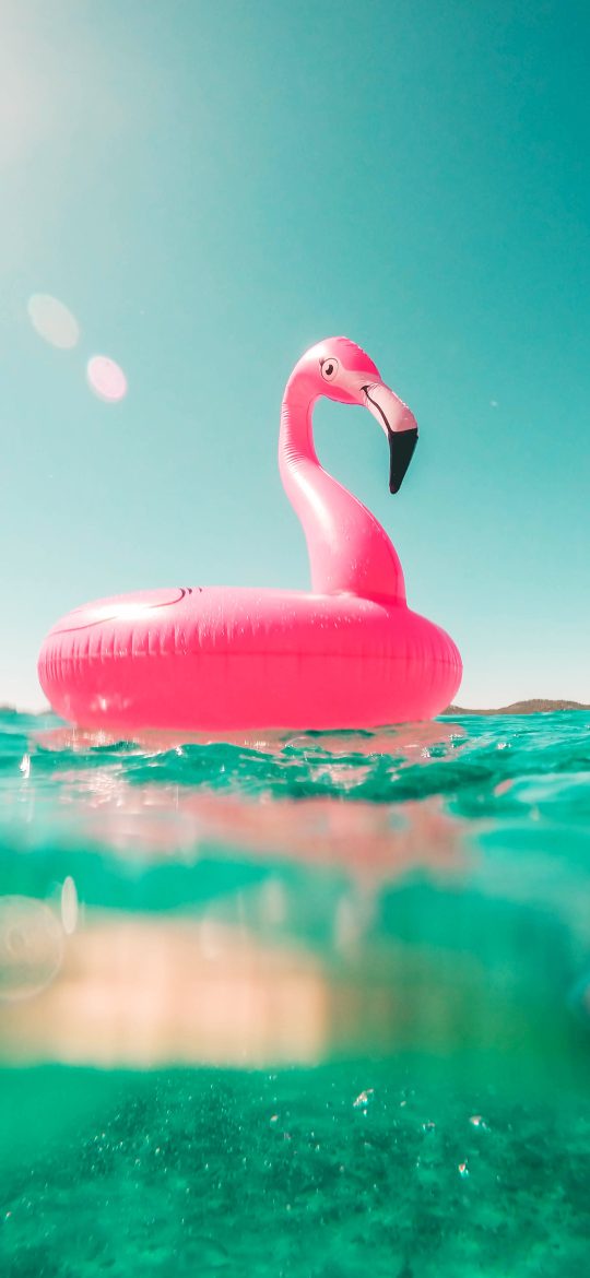 Pink flamingo pool float in clear turquoise sea beneath a pale sky