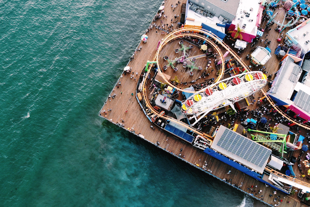 Overhead view of Pacific Park with the Ferris wheel, roller coaster, wooden pier and green Pacific Ocean