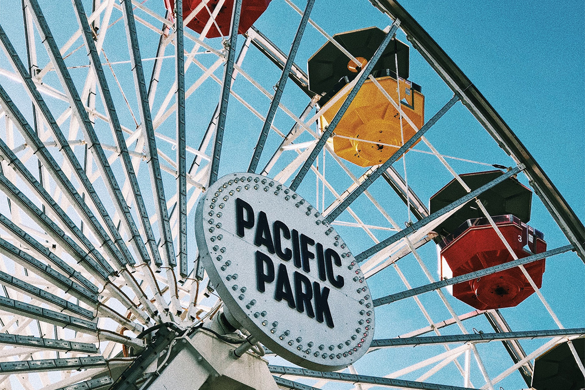 Pacific Park sign framed by the white spokes and colorful gondolas of the Pacific Wheel
