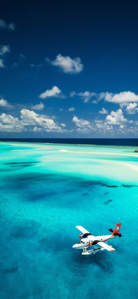 Small red and white seaplane above a blue tropical lagoon