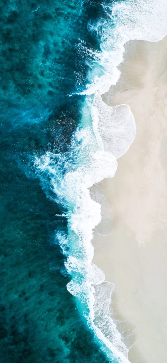 Aerial beach wallpaper with white waves meeting a narrow strip of light sand