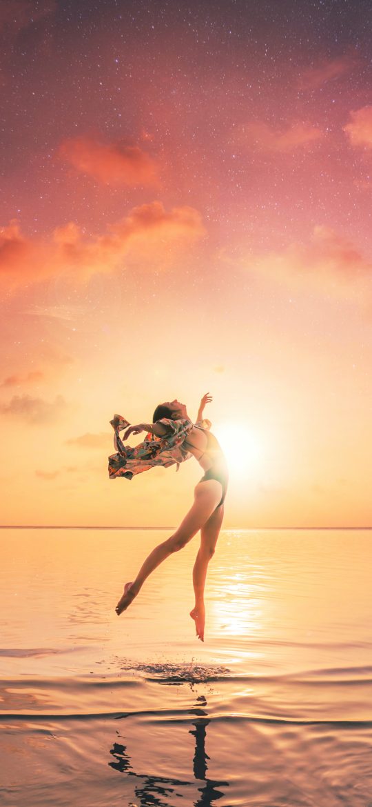 Woman moving above shallow water beneath a warm sunset sky